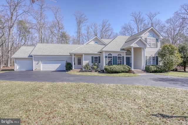 traditional-style house featuring aphalt driveway, an attached garage, a shingled roof, and a front yard