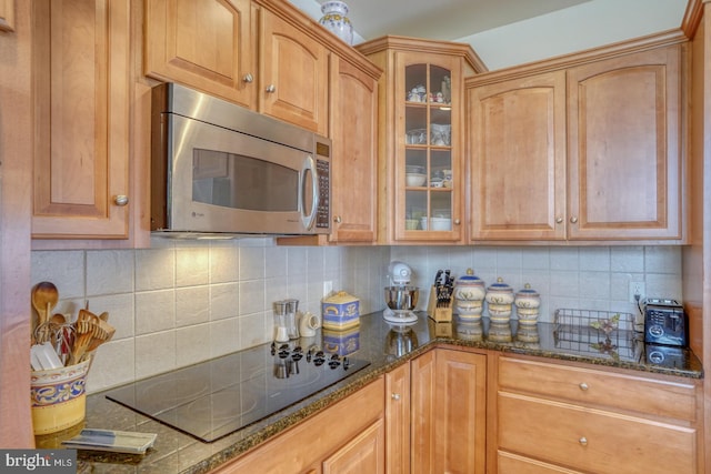 kitchen featuring black electric cooktop, dark stone counters, tasteful backsplash, stainless steel microwave, and glass insert cabinets