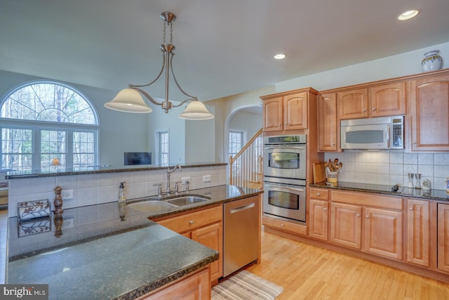 kitchen with light wood-style flooring, decorative backsplash, appliances with stainless steel finishes, a sink, and dark stone counters