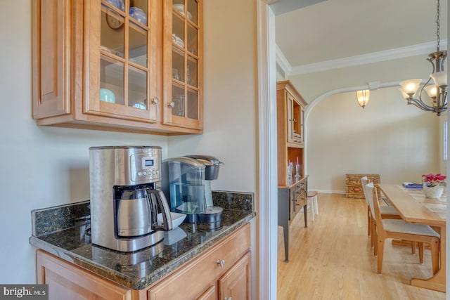 kitchen with arched walkways, light wood-style flooring, ornamental molding, dark stone counters, and glass insert cabinets