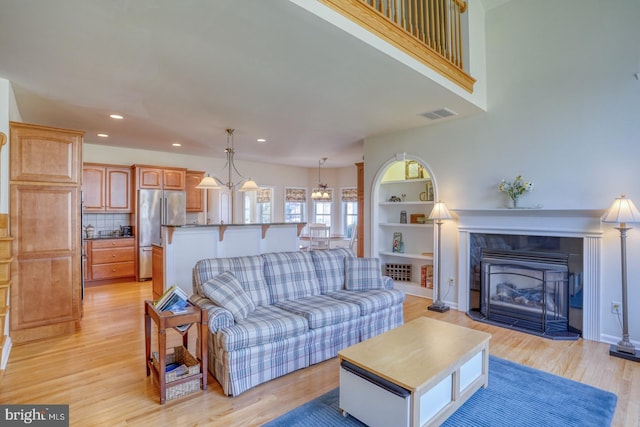 living room with light wood-style flooring, recessed lighting, visible vents, built in features, and a tiled fireplace