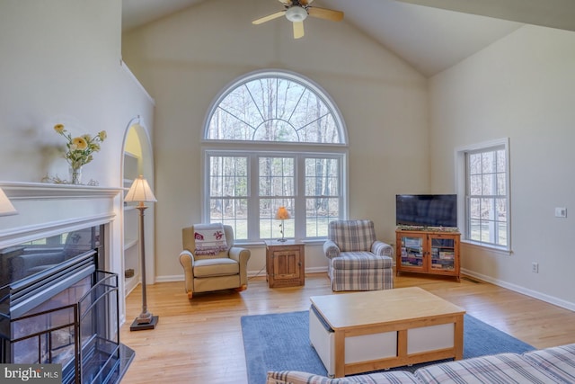 living area with high vaulted ceiling, a fireplace, and light wood-style flooring