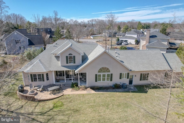 rear view of house featuring a residential view, roof with shingles, a patio, and a lawn