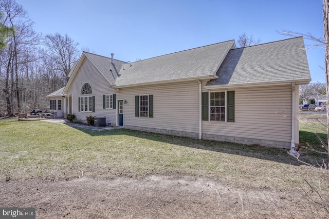 rear view of property with central air condition unit, a patio area, a shingled roof, and a yard