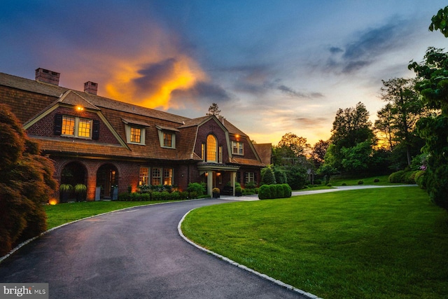 shingle-style home featuring driveway, a front lawn, a chimney, and a gambrel roof