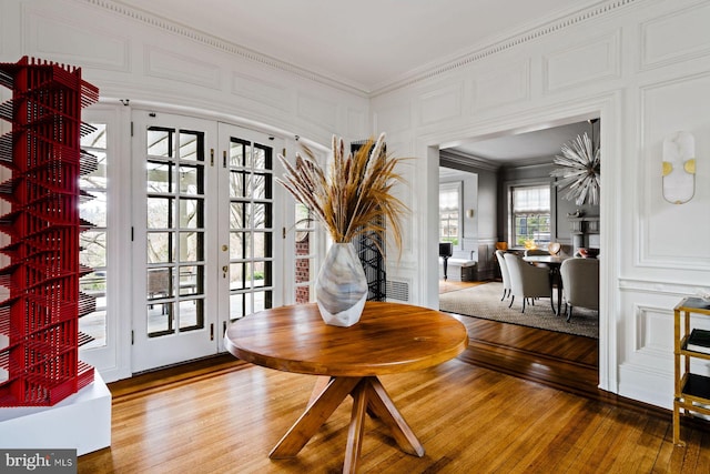 entrance foyer with french doors, ornamental molding, light wood-type flooring, and a decorative wall