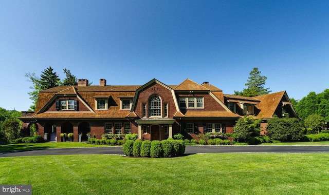 shingle-style home with a chimney, a front lawn, aphalt driveway, and a gambrel roof