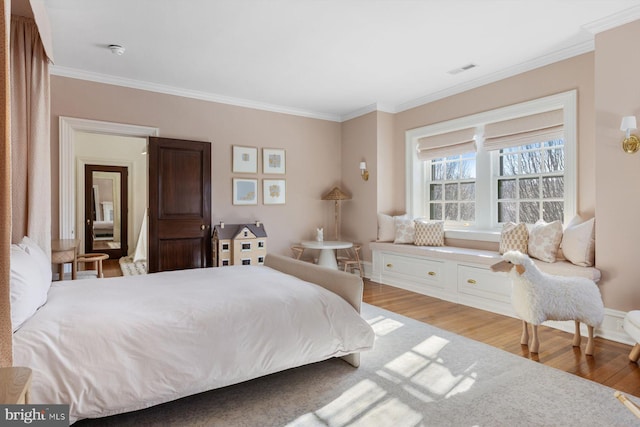 bedroom with wood finished floors, visible vents, and crown molding