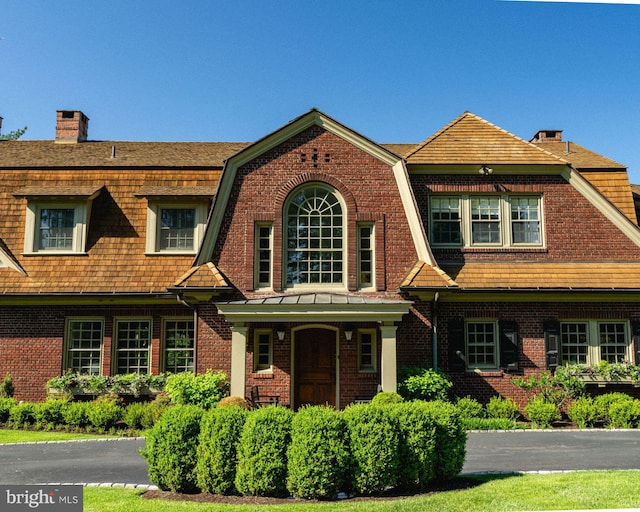 shingle-style home featuring brick siding, a chimney, and a gambrel roof