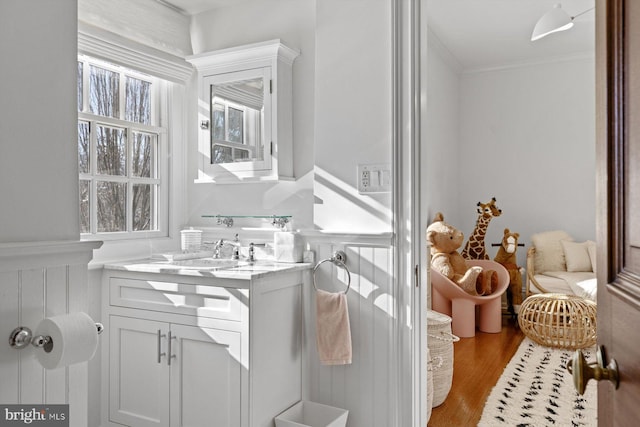 bathroom with ornamental molding, a wainscoted wall, vanity, and wood finished floors