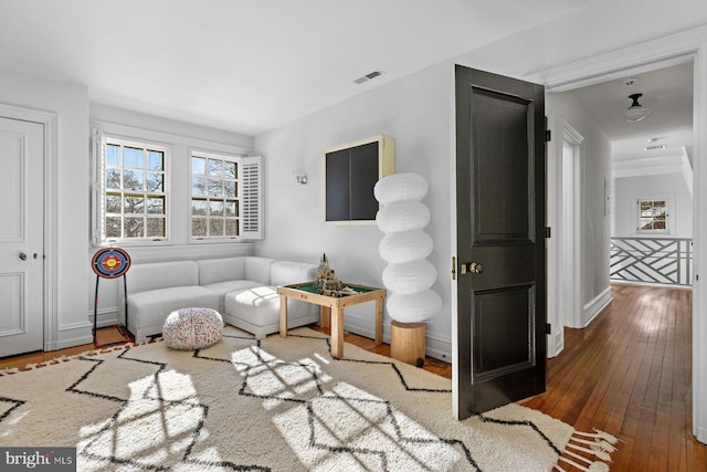 living area with an upstairs landing, wood-type flooring, visible vents, and baseboards