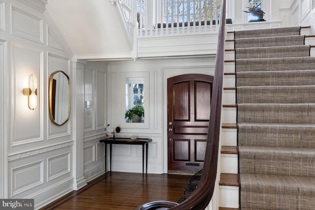 entrance foyer with lofted ceiling, stairs, a decorative wall, and dark wood-style flooring