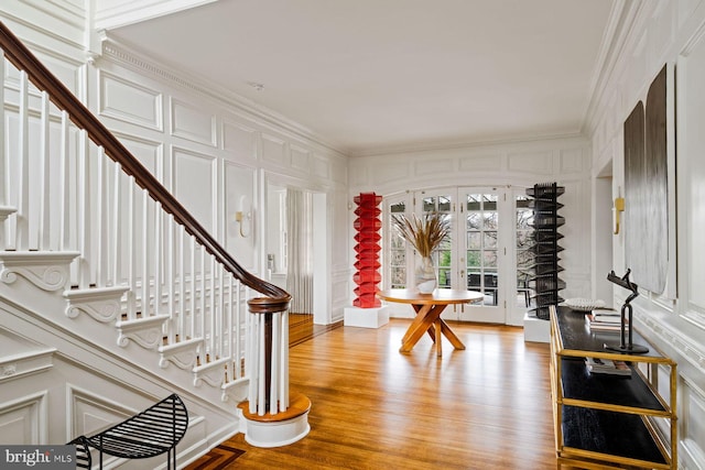 foyer featuring stairs, french doors, a decorative wall, and crown molding