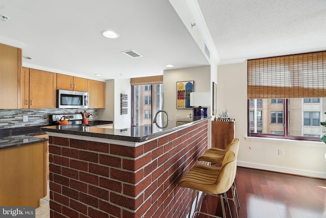 kitchen featuring visible vents, a kitchen breakfast bar, backsplash, wood finished floors, and stainless steel appliances