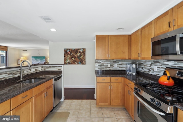 kitchen with light tile patterned floors, dark stone counters, a sink, decorative backsplash, and appliances with stainless steel finishes