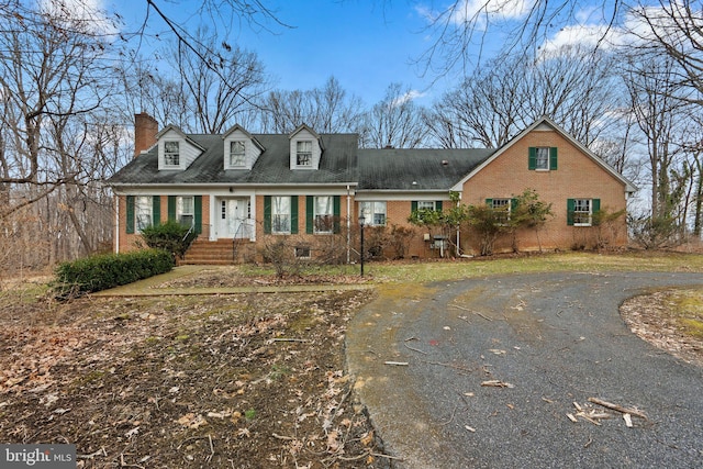 new england style home featuring brick siding, driveway, and a chimney