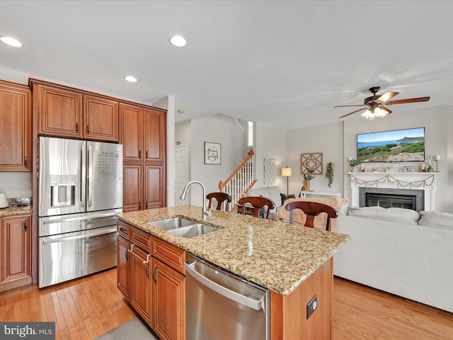 kitchen featuring light wood-style flooring, a fireplace, a sink, open floor plan, and appliances with stainless steel finishes