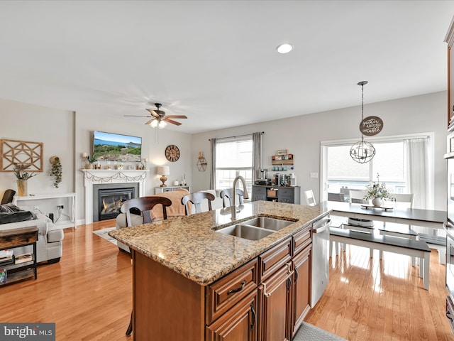 kitchen with a breakfast bar, brown cabinets, a glass covered fireplace, a sink, and dishwasher