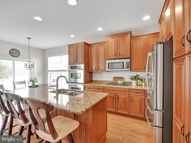 kitchen with light stone counters, light wood finished floors, stainless steel appliances, recessed lighting, and a sink