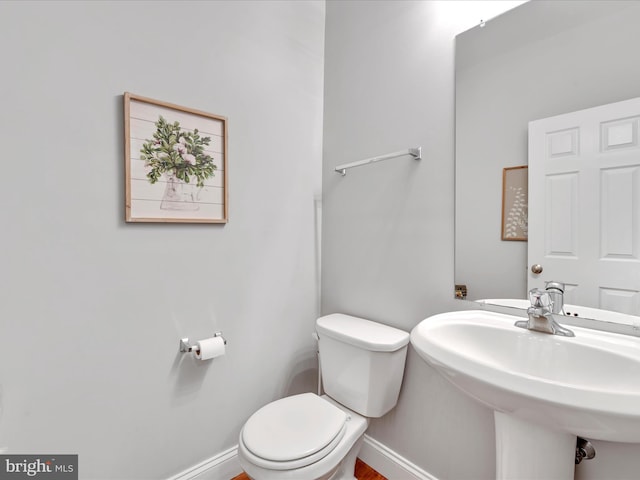 half bath featuring baseboards, a sink, and toilet