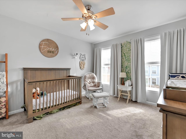 carpeted bedroom with a crib, a ceiling fan, and baseboards