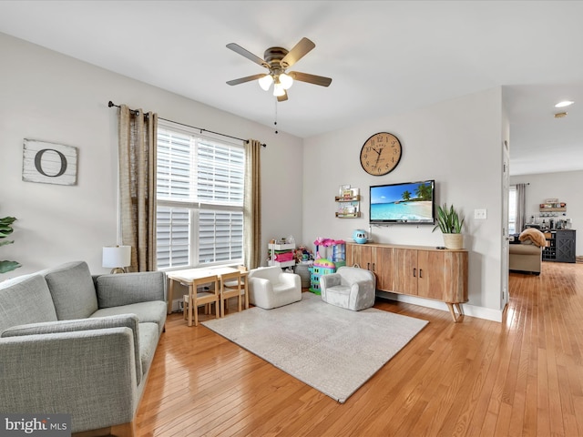 living room featuring light wood-style flooring, baseboards, and a ceiling fan