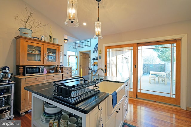 kitchen with lofted ceiling, stainless steel microwave, glass insert cabinets, wood finished floors, and a sink