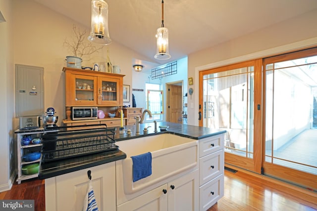 kitchen featuring dark countertops, stainless steel microwave, vaulted ceiling, and glass insert cabinets