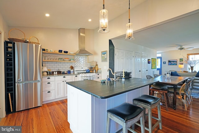 kitchen with white gas stove, a breakfast bar, a sink, wall chimney range hood, and freestanding refrigerator