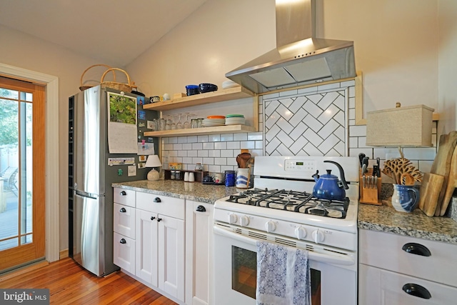 kitchen featuring white gas stove, light wood finished floors, tasteful backsplash, freestanding refrigerator, and extractor fan