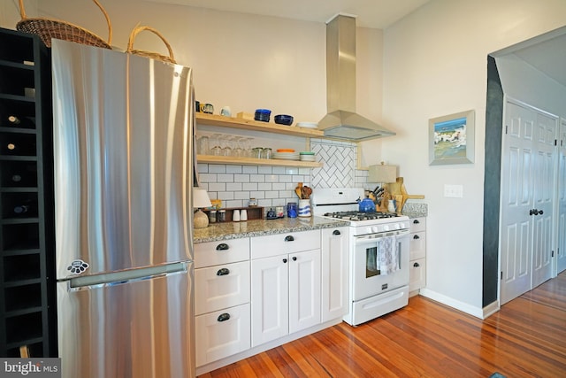 kitchen featuring white range with gas cooktop, white cabinets, wall chimney exhaust hood, wood finished floors, and freestanding refrigerator