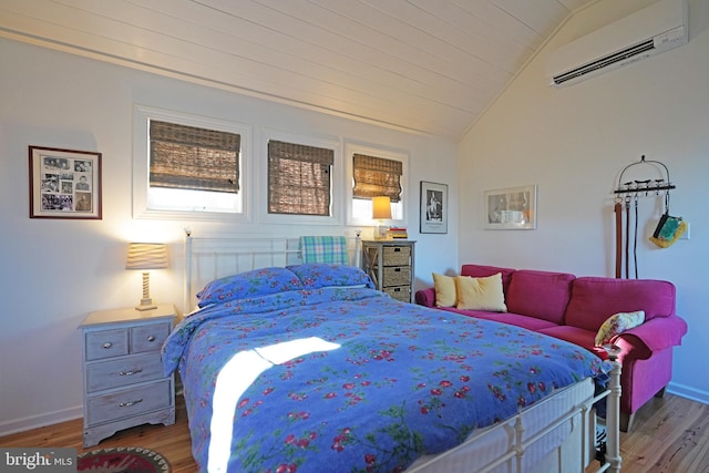 bedroom with an AC wall unit, vaulted ceiling, wood finished floors, multiple windows, and baseboards