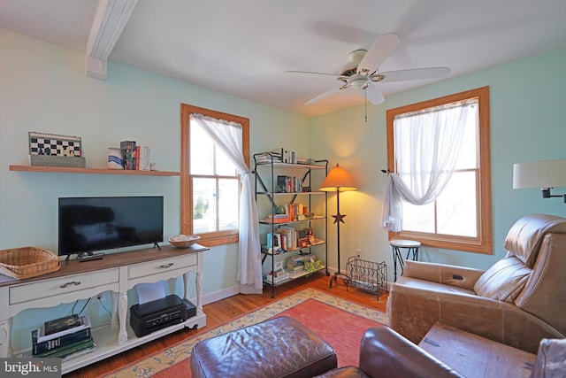 living area featuring ceiling fan, baseboards, wood finished floors, and beamed ceiling