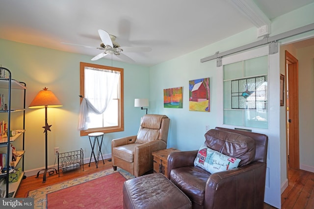 sitting room with a ceiling fan, wood finished floors, baseboards, and a barn door