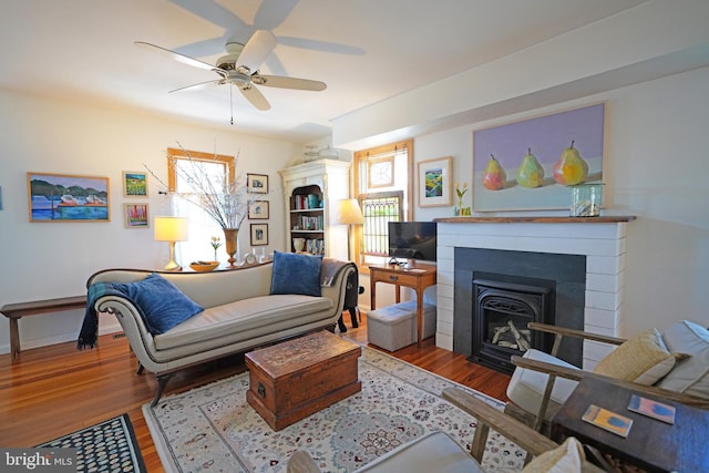 living area featuring a fireplace, a ceiling fan, and wood finished floors