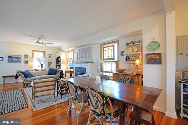 dining space with a ceiling fan, a fireplace, baseboards, and wood finished floors