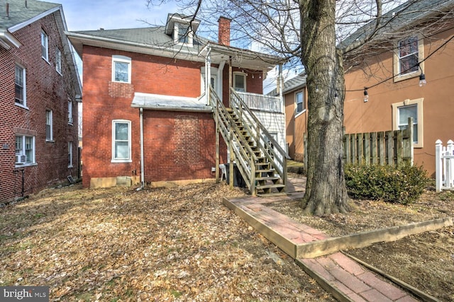 rear view of house featuring a chimney, stairway, fence, and brick siding