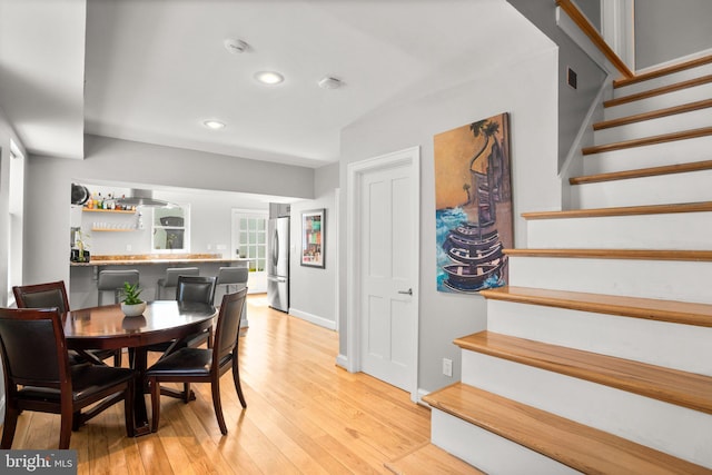 dining space featuring bar area, baseboards, stairway, light wood-type flooring, and recessed lighting