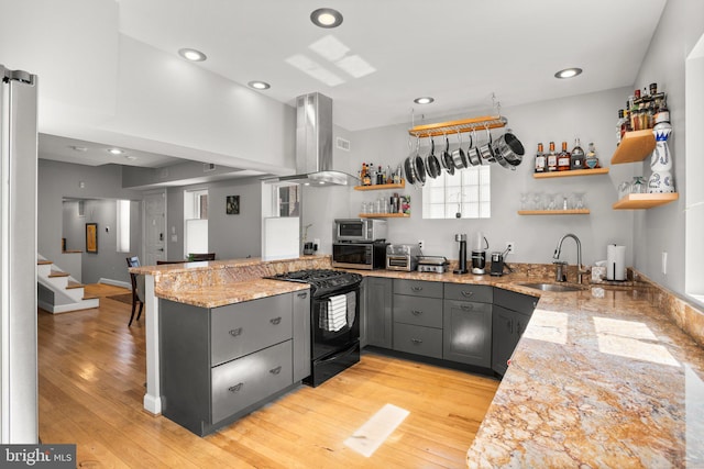 kitchen featuring gray cabinetry, open shelves, island exhaust hood, gas stove, and a sink