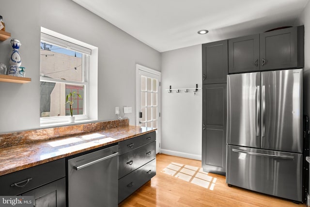 kitchen featuring light stone countertops, baseboards, light wood finished floors, stainless steel appliances, and dark cabinets