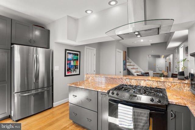 kitchen featuring light stone countertops, range with gas stovetop, light wood-style flooring, gray cabinets, and freestanding refrigerator