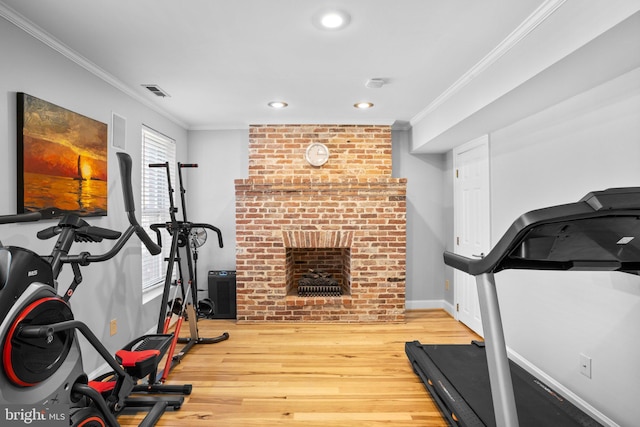 exercise room with visible vents, wood finished floors, a fireplace, crown molding, and baseboards