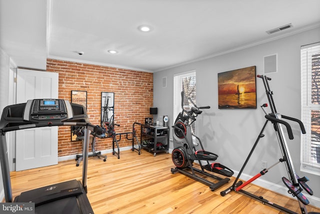 workout room with visible vents, brick wall, baseboards, ornamental molding, and wood finished floors