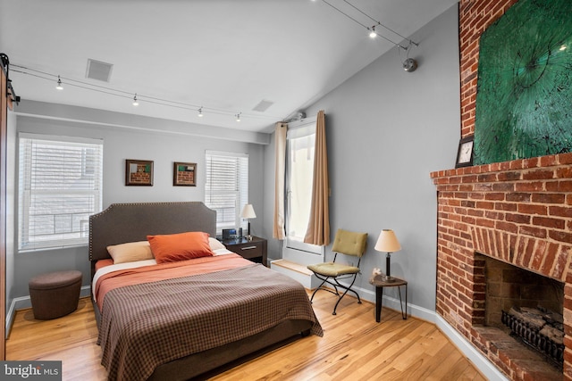 bedroom with light wood-type flooring, visible vents, rail lighting, baseboards, and a brick fireplace