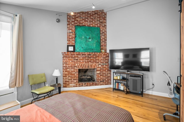 bedroom with track lighting, a brick fireplace, baseboards, and wood finished floors