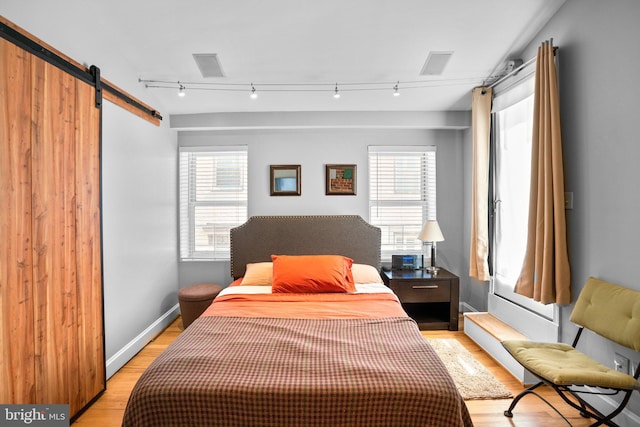 bedroom with a barn door, multiple windows, light wood-style floors, and baseboards