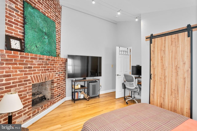 bedroom featuring wood finished floors, a barn door, rail lighting, baseboards, and a brick fireplace