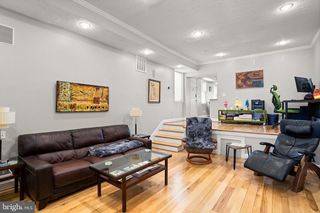 living area with visible vents, light wood-type flooring, ornamental molding, recessed lighting, and a textured ceiling