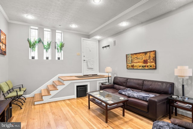 living room featuring visible vents, baseboards, hardwood / wood-style floors, ornamental molding, and a textured ceiling