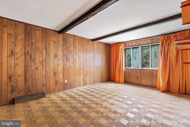 unfurnished room featuring baseboards, wooden walls, visible vents, and beamed ceiling